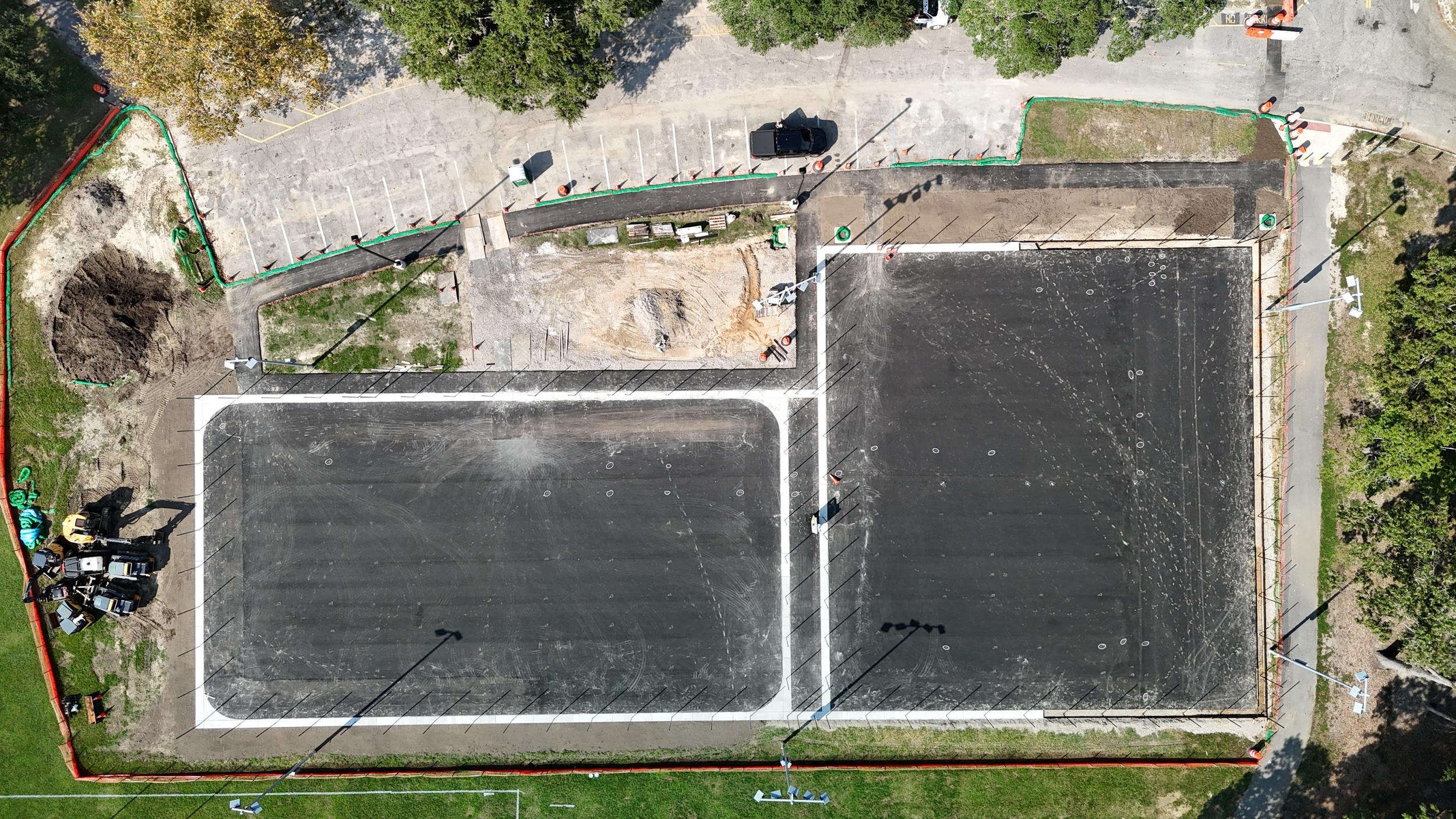 New paving and perimeter concrete define the courts while fencing and surrounding sitework continue.