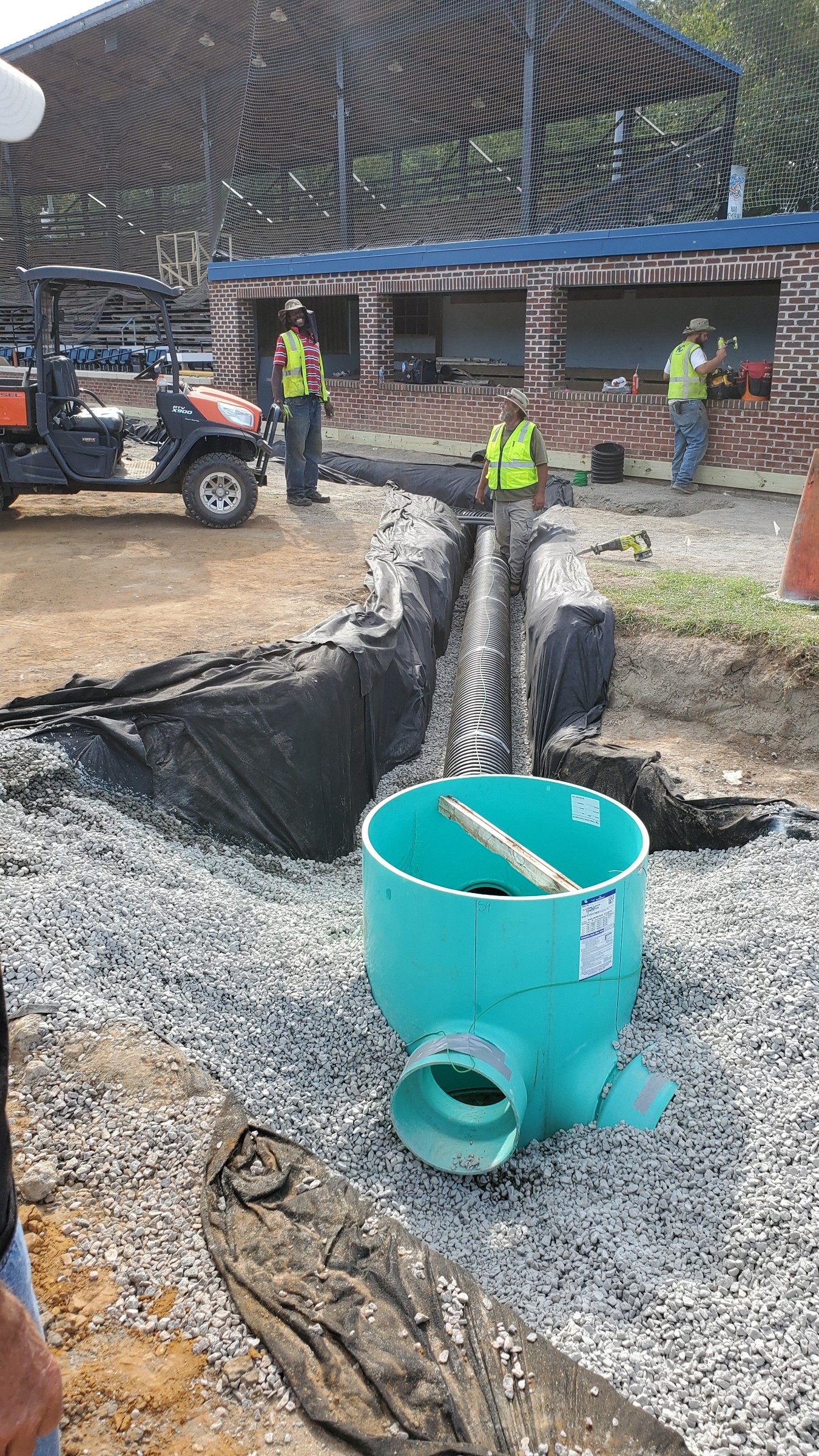 Drainage structure and pipe set in stone bedding within the fabric-lined trench.